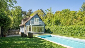 Een huis met zwembad, omgeven door een verzorgd gazon en weelderige begroeiing.