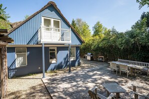 Una casa blu con un balcone, un patio con mobili in legno e un'area giardino.