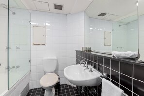 Een badkamer met een douchecabine van glas, een wit toilet, een wastafel met een zwart aanrechtblad en een spiegel boven de wastafel.