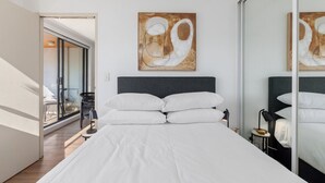Una habitación de hotel moderna con una cama grande, vistas a través de un ventanal y una obra de arte abstracta en la pared.