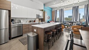 A modern kitchen with stainless steel appliances, a central island with stools, and a dining area with a view of the city. - Industrial Loft - Sleeps 10 - FREE Valet (Dallas)