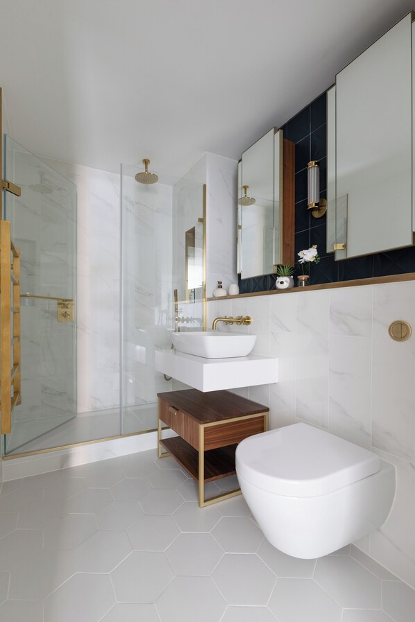 A modern bathroom with a glass shower enclosure, a white sink with gold fixtures, and a white toilet.