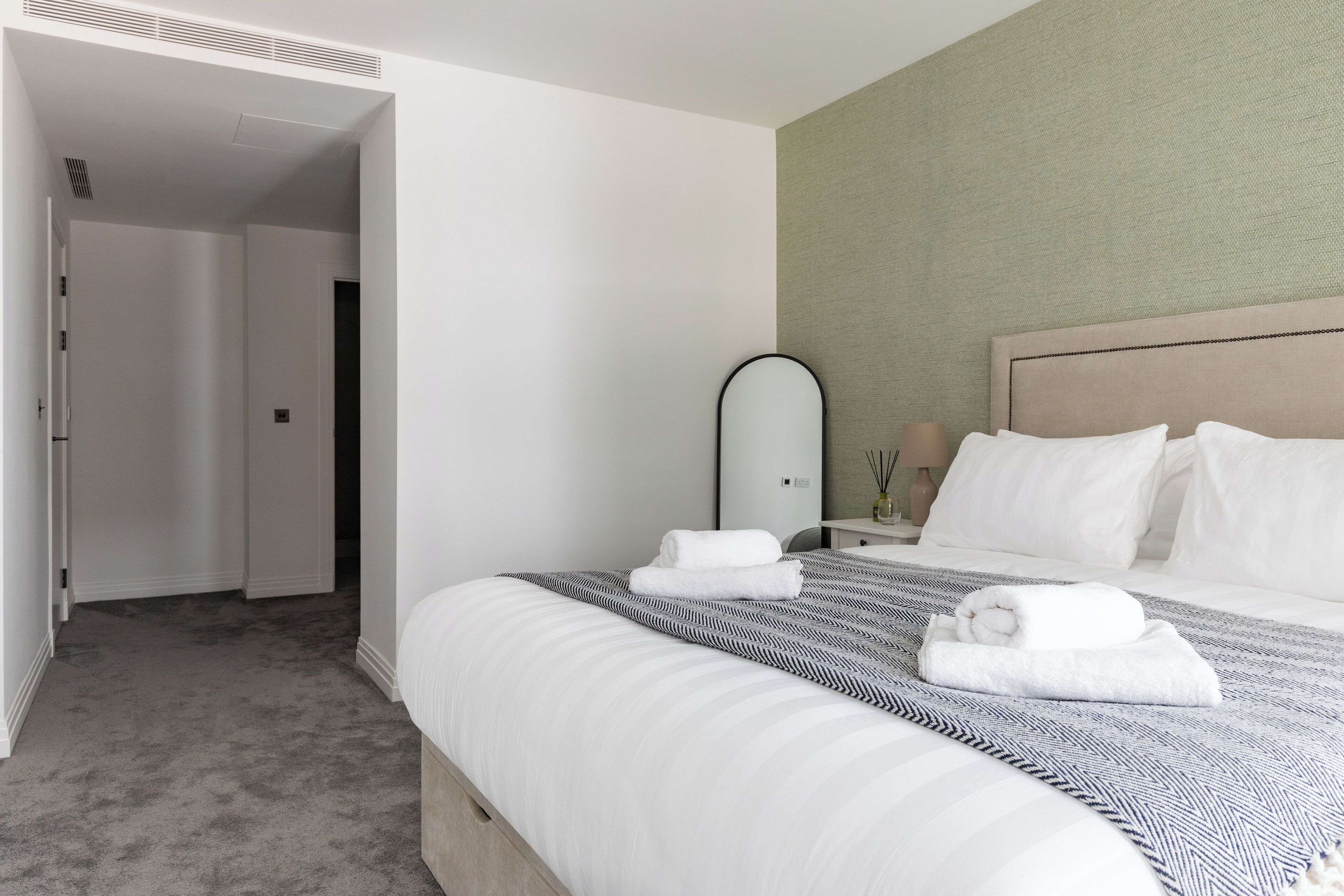 A hotel room with a large bed, a bedside table with a lamp, and a mirror on the wall.