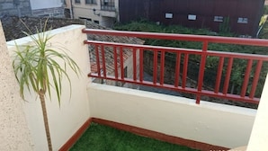 Un balcon avec une balustrade rouge, une petite plante en pot et une vue sur les immeubles voisins.