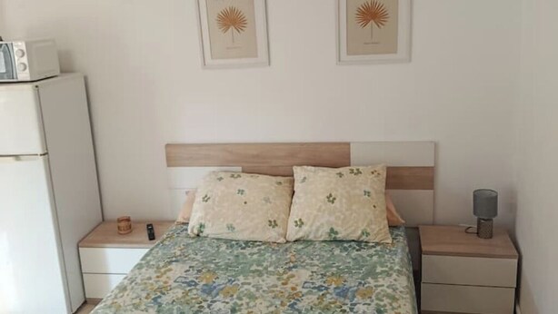 Une chambre à coucher comprenant un lit, deux tables de chevet, une lampe de chevet, un four à micro-ondes et deux tableaux encadrés accrochés au mur.
