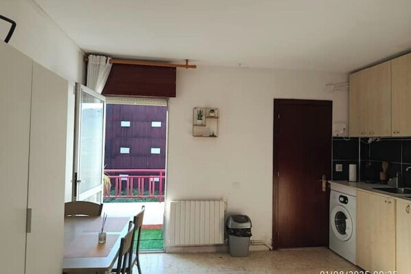 A compact kitchen with a washing machine, a radiator, and a dining area with a table and chairs. - Loft Solpor - Your haven of calm in front of the sunset (Marín)