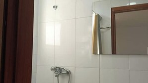 Une salle de bain avec des carreaux blancs, une douche, un miroir et une porte en bois.