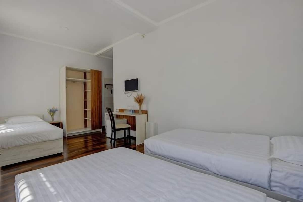 A hotel room with three beds, a desk with a chair, a TV, and a wardrobe.