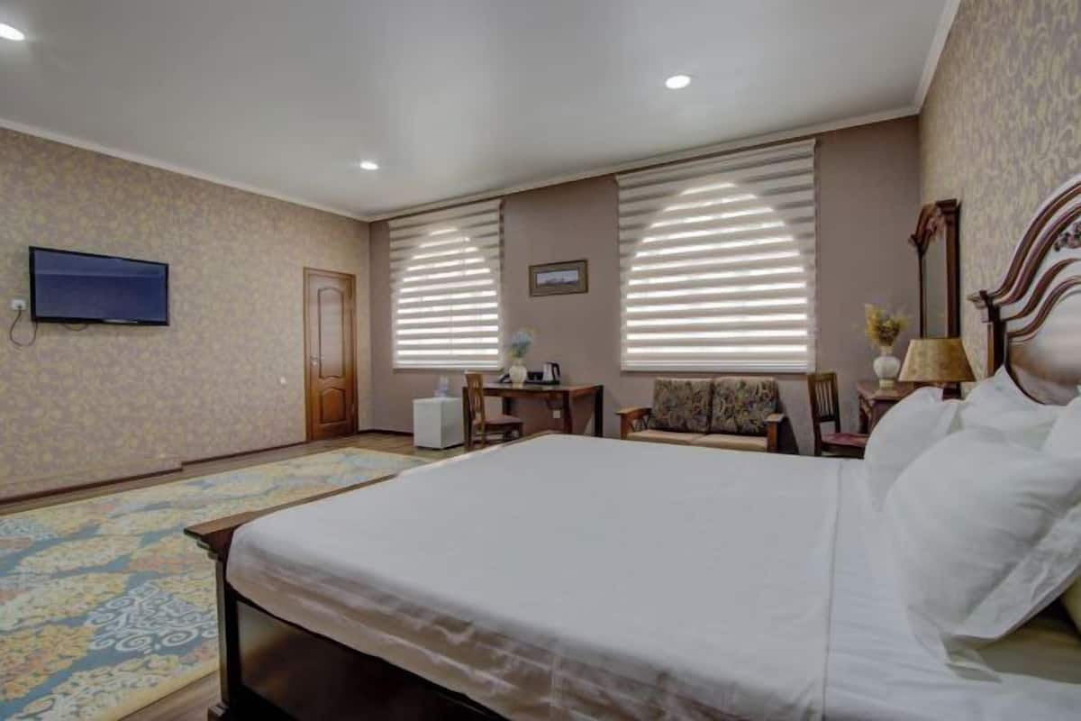 A hotel room with a large bed, a desk, a chair, a television, and a window with blinds.