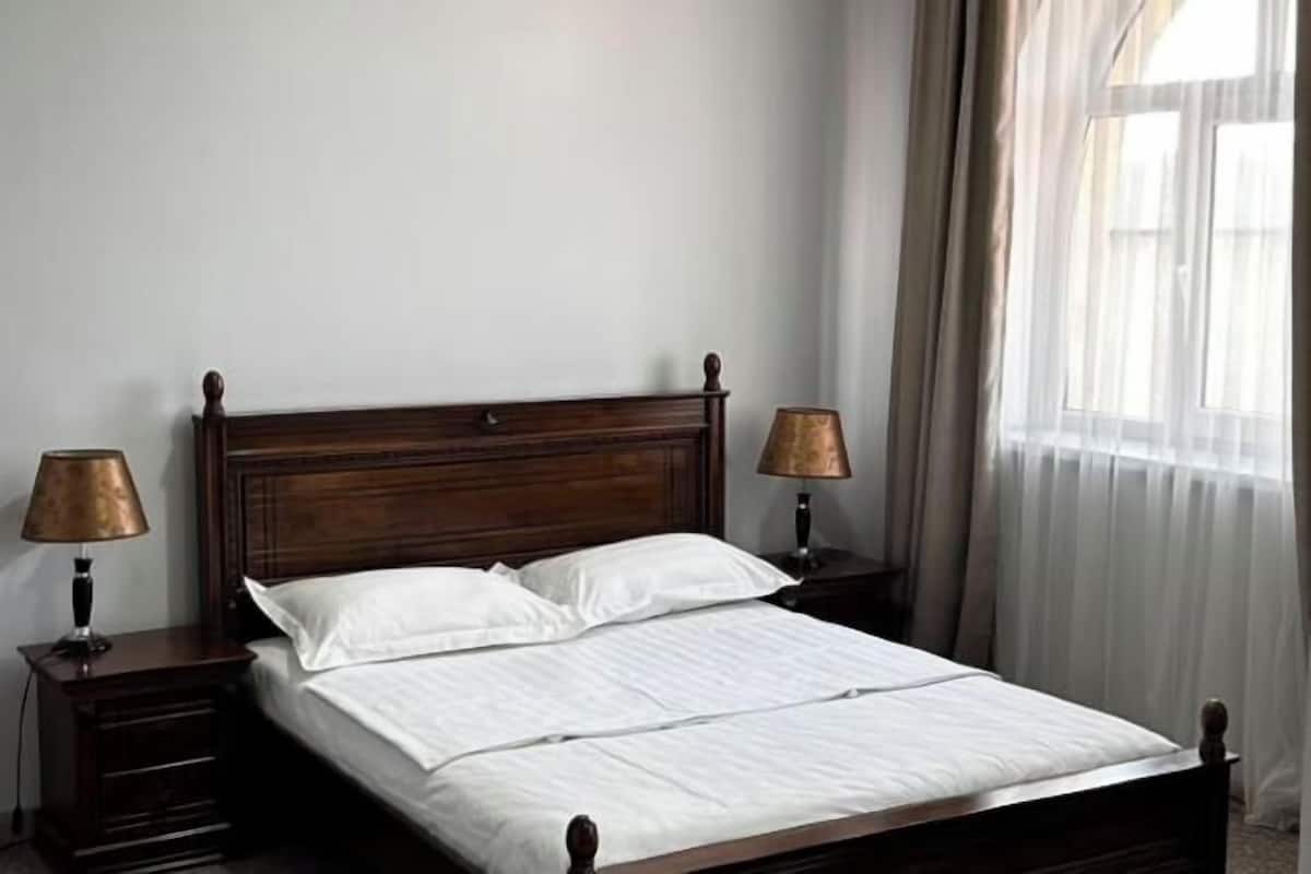 A neatly made bed with white linens, two bedside lamps, and a wooden headboard.