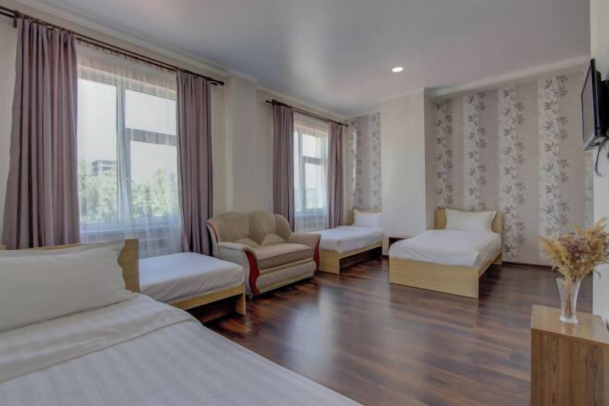 A hotel room with two single beds, a sofa, a TV, and a wooden desk.