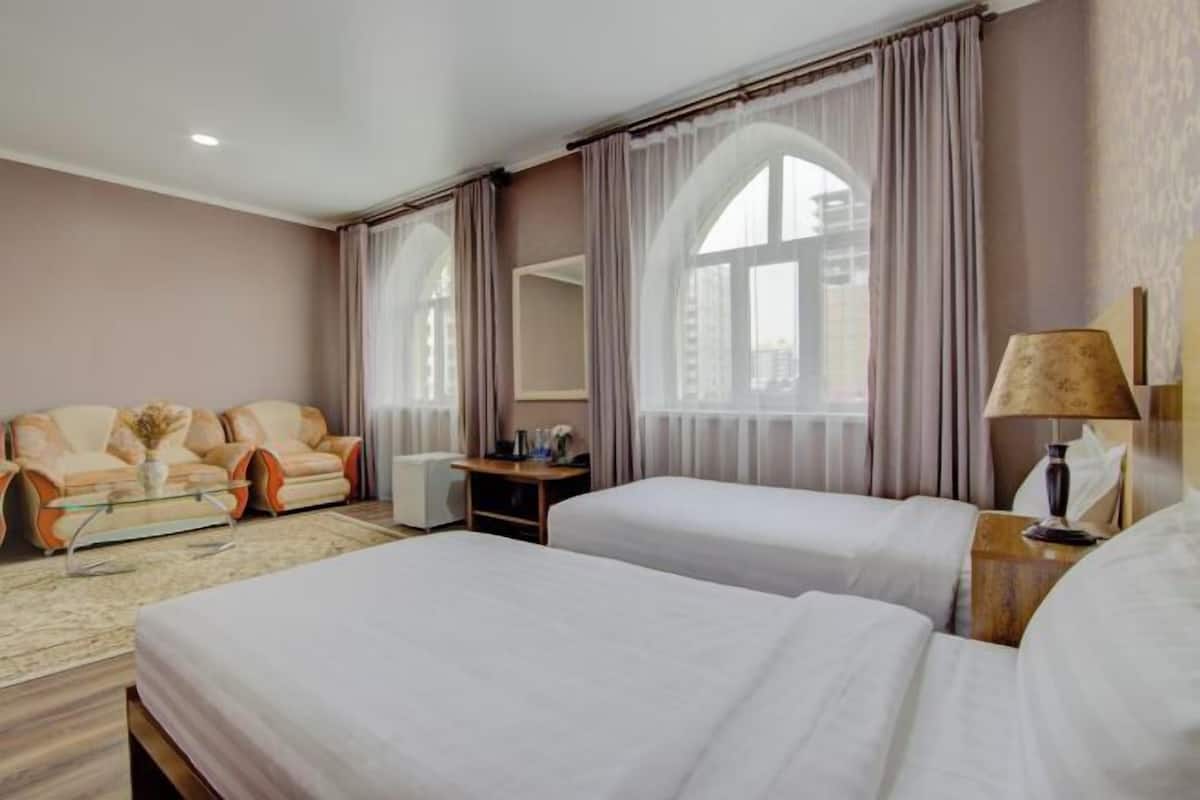 A hotel room with two beds, a sofa, a desk, and a large window with curtains.