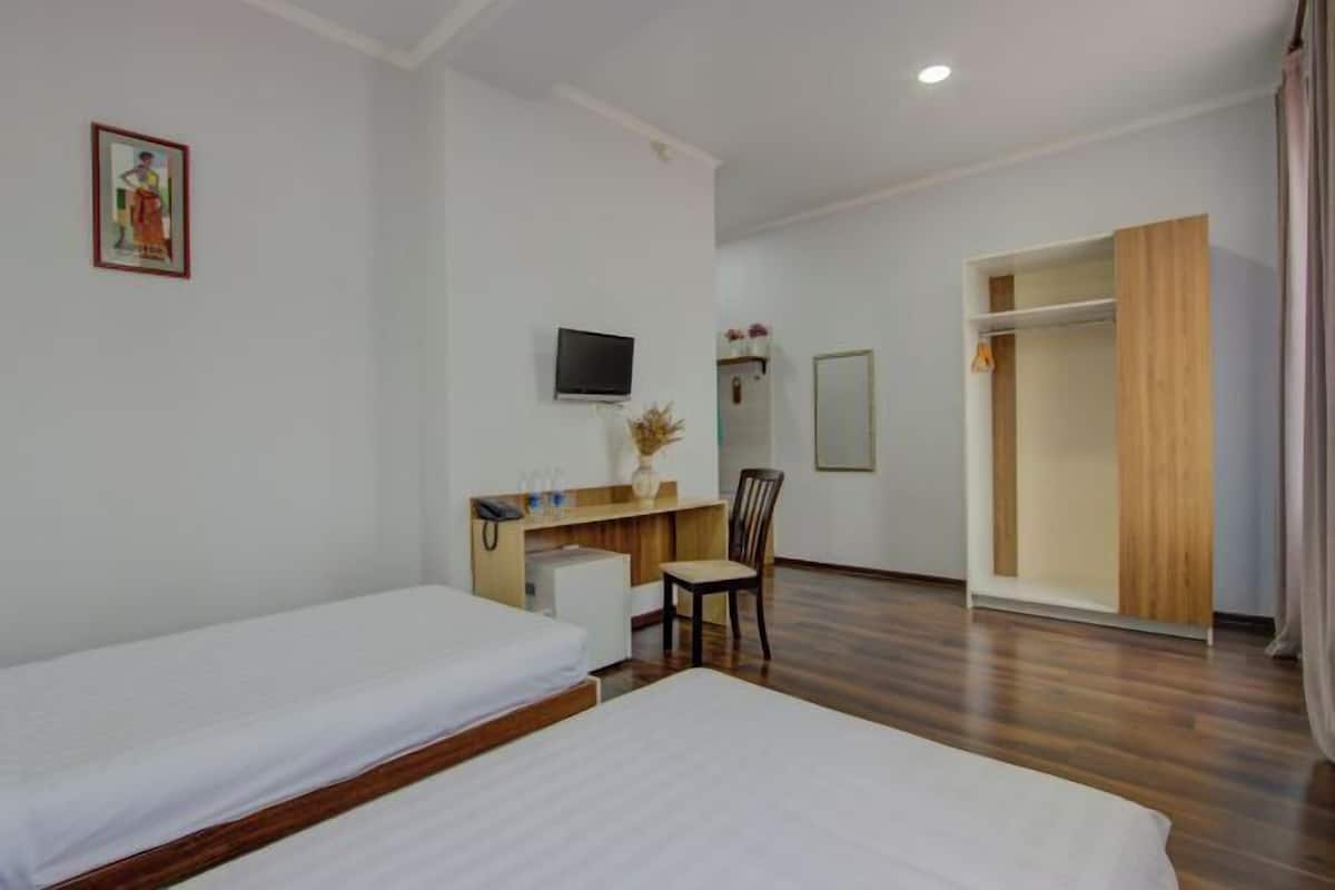A hotel room with two beds, a desk with a chair, a TV, and a wardrobe.