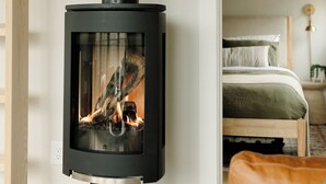 Une chambre moderne avec un poêle à bois noir, un lit avec une literie verte et un plafond en bois.