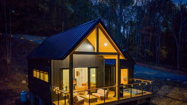 Une cabane dotée d’une terrasse en bois, de grandes fenêtres et d’un balcon.