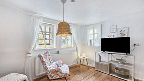 A room with a television, a rocking chair, a white radiator, and a window with curtains.