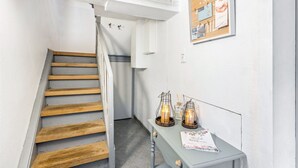A staircase with wooden steps and metal railings, a wall-mounted corkboard with pinned items, and a small table with candles and a magazine.