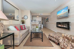 A living room with a sofa, a coffee table, a TV, and a fireplace. - Oceanfront King, Walk-in-Shower, Fireplace, Heated Pools, Exc Walkability (Myrtle Beach)