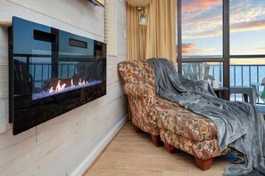 Ein Wohnzimmer mit einem an der Wand befestigten Flachbildfernseher, einer Couch mit gemustertem Bezug und Meerblick durch große Fenster.
