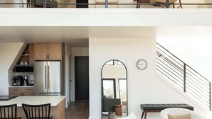 Amplia sala de estar con techo alto, cocina equipada con electrodomésticos modernos y una escalera que conecta dos niveles.