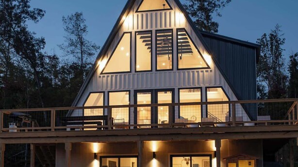 Una casa moderna con una amplia terraza, mobiliario exterior y una fogata.