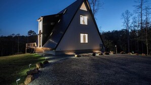 Una casa moderna de forma triangular con techo inclinado, una terraza de madera y un camino de entrada de grava.