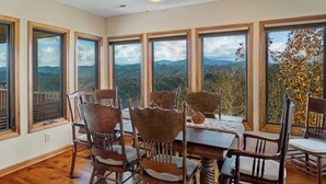 Un coin repas avec une table et des chaises, de grandes fenêtres offrant une vue sur les montagnes et un ventilateur de plafond.
