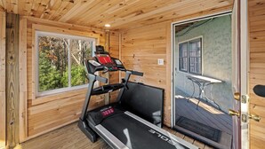 L’intérieur d’un chalet en bois est aménagé avec un tapis de course, une fenêtre donnant sur les arbres et une porte menant à l’extérieur.