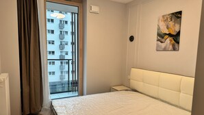 Ein Schlafzimmer mit einem Bett, einem Nachttisch, einem Fenster mit Vorhängen und einer Wand-Klimaanlage.