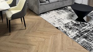 Ein modernes Wohnzimmer mit einem grauen Sofa, zwei Sesseln, einem schwarzen Couchtisch und einem gemusterten Teppich.