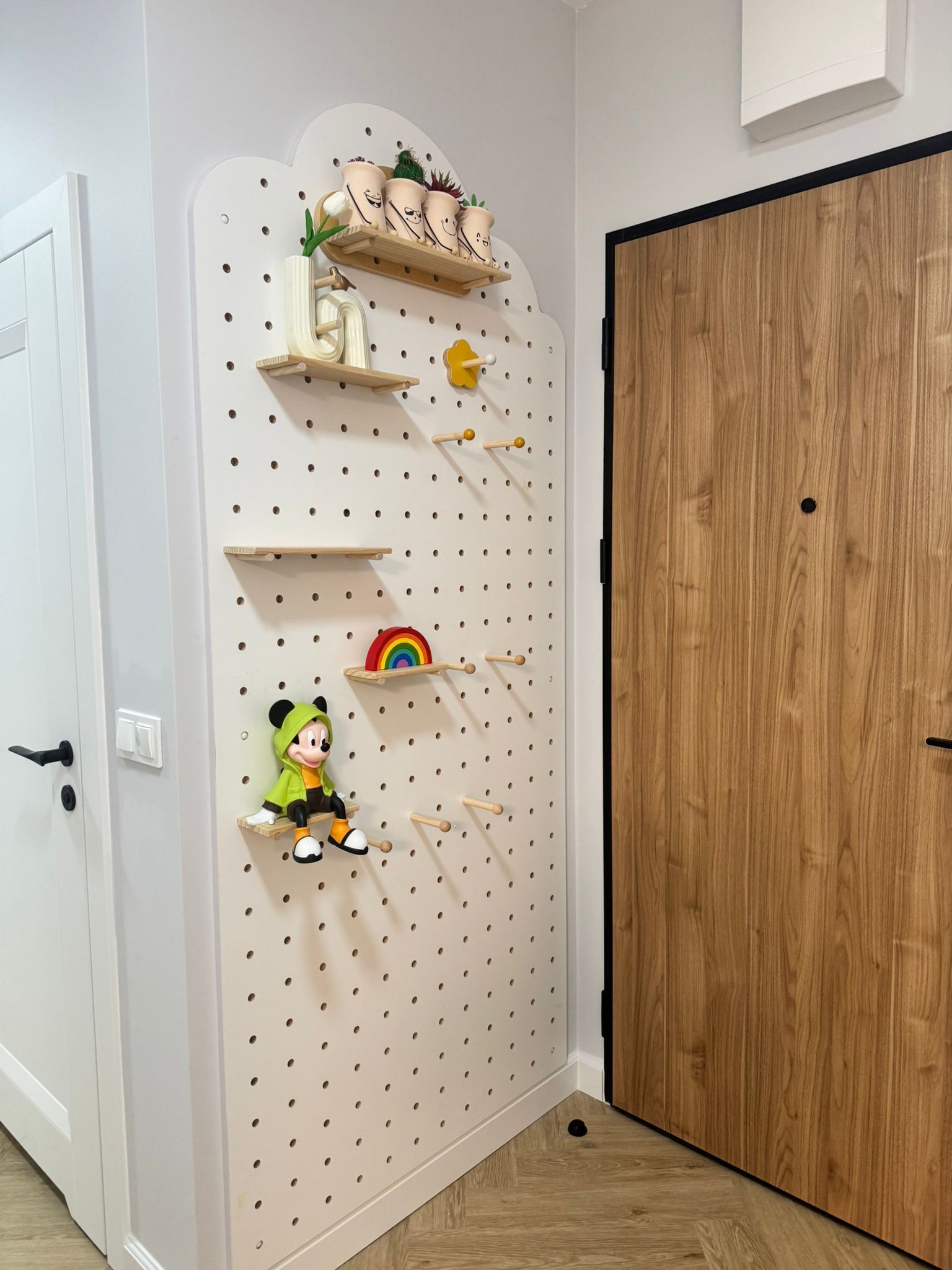 A pegboard wall with shelves and hooks, a wooden door, and a small Mickey Mouse figure.