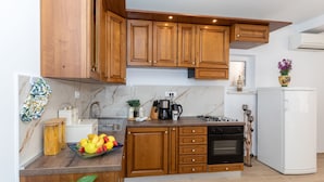 A modern kitchen with wooden cabinets, a marble countertop, a built-in oven, and a white refrigerator. - Apartment Zelenika Villa by Villas Guide (Ploce)