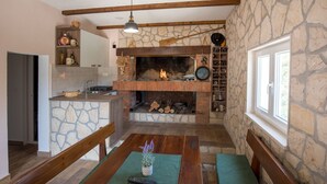 A cozy kitchen with a stone wall, a fireplace, and a dining area with a wooden bench and table. - Apartment Zelenika Villa by Villas Guide (Ploce)