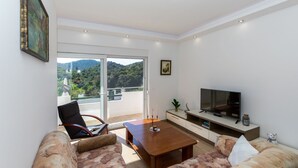 A modern living room with a sofa, a coffee table, a TV, and a balcony with a scenic view. - Apartment Zelenika Villa by Villas Guide (Ploce)