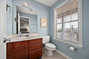 Een badkamer met een houten wastafelmeubel, een witte wastafel, een toilet en een raam met blinds.