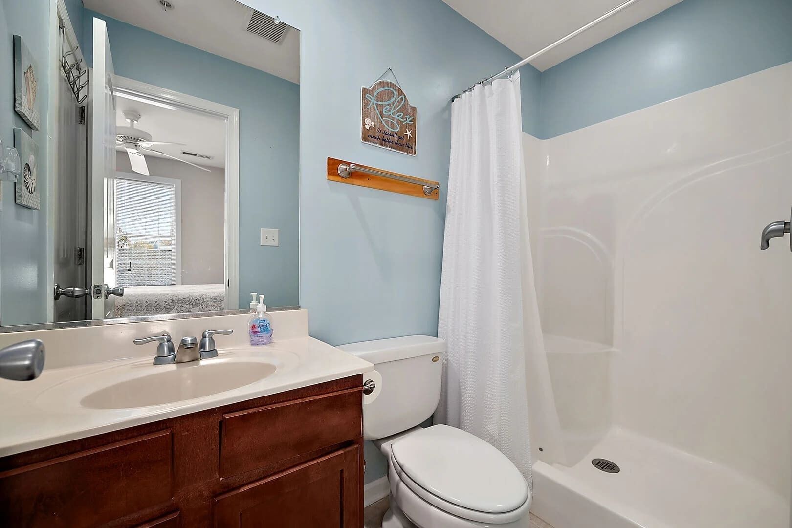 A bathroom with a white sink, vanity, and toilet. There is a shower curtain and a towel rack on the wall.