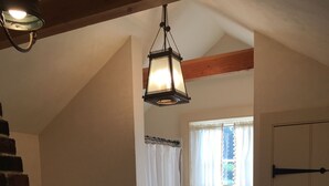 A room with a brick fireplace, a hanging lantern, a window with curtains, and a door. - Charming cottage on goat farm in picturesque Westport (Westport)