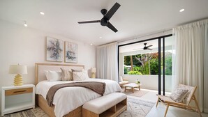 A modern bedroom with a large bed, bedside tables, a ceiling fan, and a view of greenery through large windows. - Sorrento 10 3 Bedroom Villa (Gibbes)