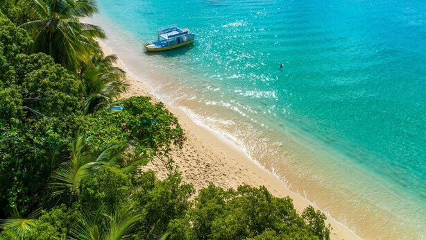 A beach with clear turquoise water, a boat, and dense tropical vegetation.