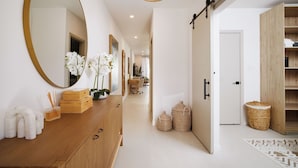 A modern hallway with a wooden dresser, a large mirror, and a sliding door leading to a room.