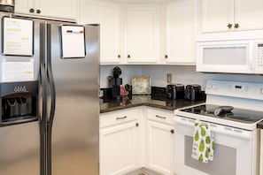 A kitchen with white cabinets, a stainless steel refrigerator, a microwave, a stove, and a coffee maker. - Cozy Family Retreat Steps To Beach Pool / Hot 2 Bedroom Apts (South Padre Island)