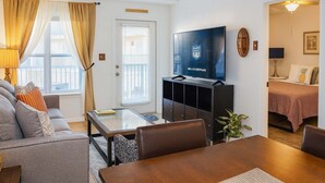 A modern living room with a sofa, a coffee table, a TV on a stand, and a dining area with a table and chairs.