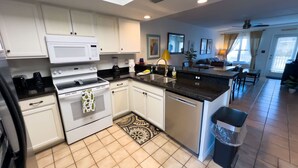 A modern kitchen with white cabinets, a stove, and a sink. There is a dining area with a table and chairs.