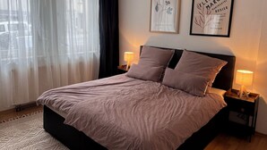 A bedroom with a bed, two bedside tables with lamps, a window with sheer curtains, and two framed pictures on the wall. - 300 MBit WLAN | directly at Marienplatz | first floor | subway (Stuttgart)