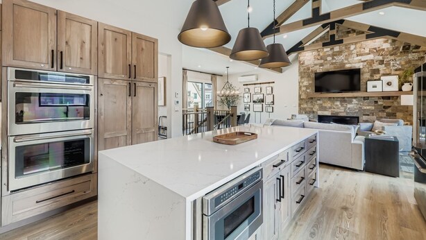 A modern kitchen with built-in ovens, a large island, pendant lighting, and a stone accent wall. - 37 Alcove 3 Bedroom Townhouse (Keystone)
