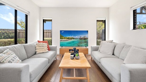 A modern living room with two grey sofas, a wooden coffee table, and a large flat-screen TV on a stand. - Bright 2-bed Glenroy Home With Courtyard (Melbourne)