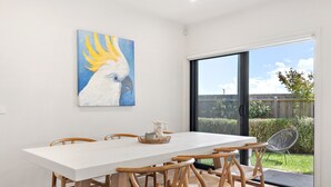 A dining area with a white table, wooden chairs, and a glass door leading to a garden. - Bright 2-bed Glenroy Home With Courtyard (Melbourne)