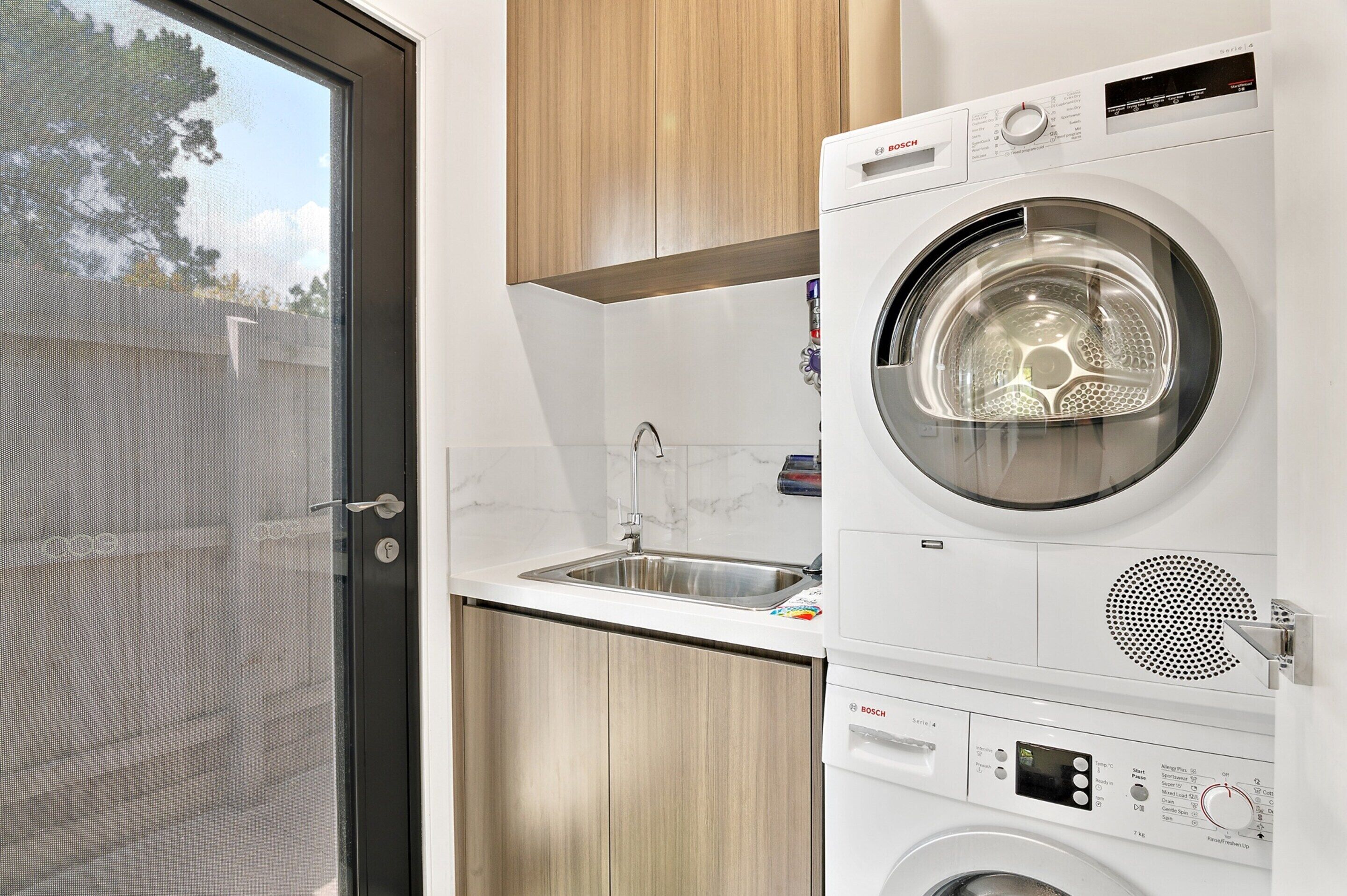A compact laundry room with a Bosch washing machine, a sink, and wooden cabinets.