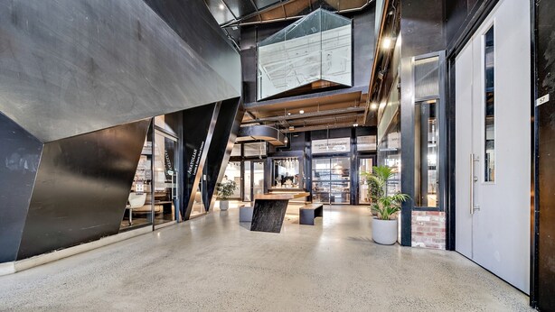 Een ruime lobby met een hoge plafond, een groot digitaal scherm en een zithoek met potplanten.