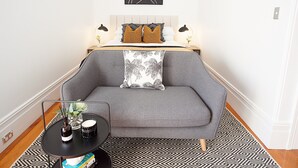 A modern bedroom with a grey sofa, patterned rug, and a small side table with books and a vase. - Perfect Located Comfy Studio With Balcony (Sydney)